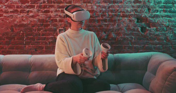 Young woman siting on the couch wearing vr goggles and husing handles to experience vr