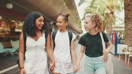 Three girls friends pre-teenage go on the street smiling and emotionally talking holding hands. Three teenagers on the outdoors in urban cityscape background - Powered by Adobe