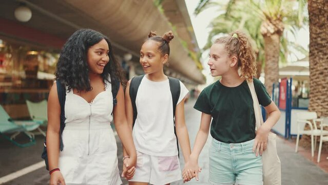 Three girls friends pre-teenage go on the street smiling and emotionally talking holding hands. Three teenagers on the outdoors in urban cityscape background