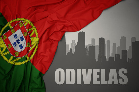 abstract silhouette of the city with text Odivelas near waving national flag of portugal on a gray background.