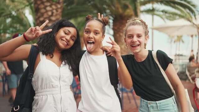 Three girls friends pre-teenage standing on the street smiling, hugging each other making faces for the camera. Three teenagers on the outdoors in urban cityscape background