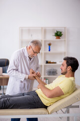 Young male patient visiting old male doctor chiropractor