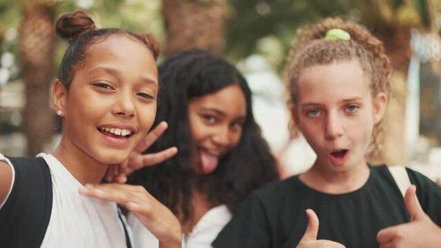 Clouse-up three girls friends pre-teenage standing on the street smiling, hugging each other making faces for the cell phone camera, selfie. Three teenagers on the outdoors 
