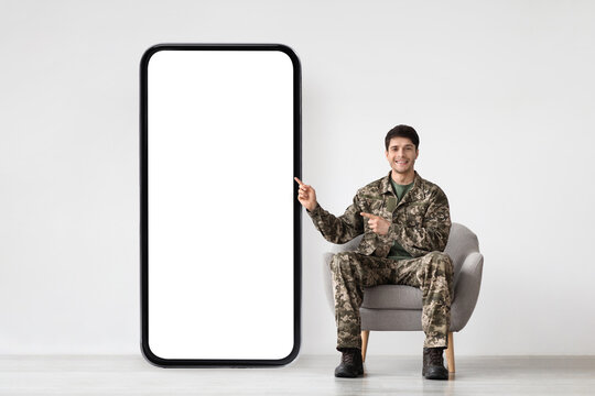 Smiling soldier in military uniform sitting by huge phone, mockup