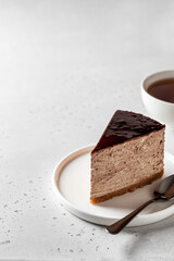 Chocolate cheesecake slice glazed with tea cup on white textured background with text space on the left