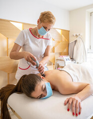 Obraz premium Young woman wearing protective mask receiving ultrasound cavitation treatment by cosmetologist in beauty center.