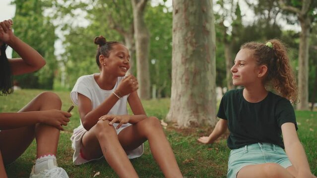 Three girls friends pre-teenage sit on the grass in the park and emotionally talking. Three teenagers on the outdoors. Camera moves around