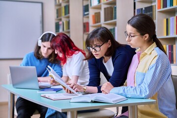 Group of teenage students and teacher study at desk in library