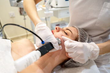 Beautician applying rejuvenation treatment on young woman face in beauty salon