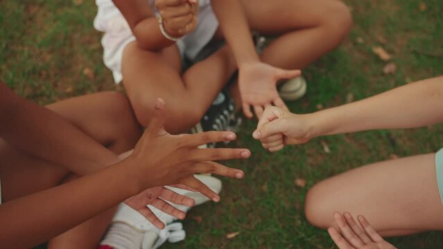 Close-up of the hands of three girls friends pre-teenage sitting on the grass in the park playing Rock-paper-scissors