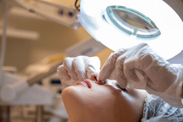 Beautician squeezing and removing manually blackhead from female client's nose and face during the cosmetic procedure in beauty salon.
