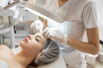 Cosmetologist squeezing acne on female patients forehead with wipes in beauty salon