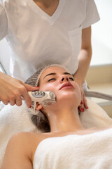 Attractive woman getting skin rejuvenation with RF lifting apparatus at professional beauty salon
