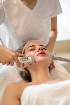 Attractive woman getting skin rejuvenation with RF lifting apparatus at professional beauty salon