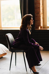 a young brunette woman in a purple pantsuit on the background of the window 