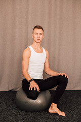 Fototapeta premium Young handsome athlete sits on a fitball in a fitness club