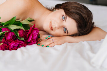 a gentle brunette woman in bed with a bouquet of peonies. morning of holiday.