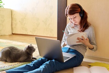 Preteen girl studying at home using laptop along with cat
