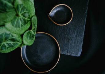 An empty ceramic black plate with gold edging on a black background. Copy of the space view from above - Image
