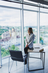 Woman manager in a jacket and glasses on her face sits on a desk at work in the office, a pensive female freelancer on project planning, doing remote work