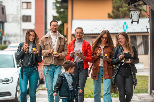 A group of young people dressed in modern clothes talks while walking around the city and eating sweets. Selective focus. High quality photo