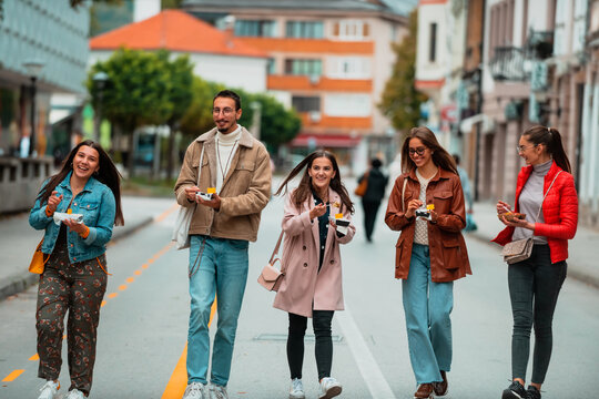 A group of young people dressed in modern clothes talks while walking around the city and eating sweets. Selective focus. High quality photo