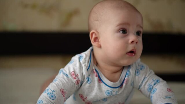 Newborn Active Baby Cute Smiling Teethless Face Portrait Early Days On Stomach Developing Neck Control. 5 Months Child On White Bed Looking on Camera. Infant, Childbirth, Parenthood, Beginning Concept