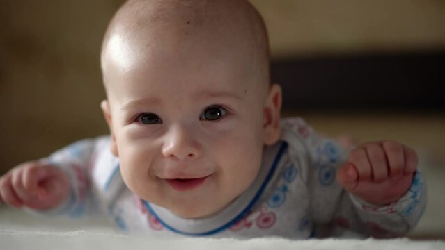 Newborn Active Baby Cute Smiling Teethless Face Portrait Early Days On Stomach Developing Neck Control. 5 Months Child On White Bed Looking on Camera. Infant, Childbirth, Parenthood, Beginning Concept