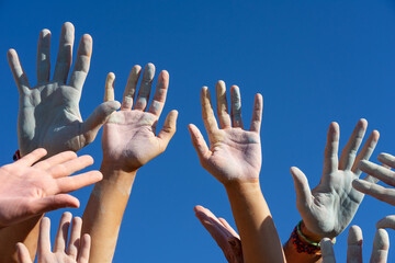 Hands of a group of people with colored chalk powder raised up against the blue sky