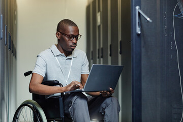 Portrait of African American man with disability using laptop in server room while working as IT...