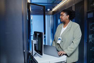 Side view portrait of African American young woman setting up server network and using laptop, copy...