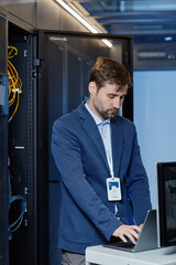 Portrait of Caucasian young man wearing blazer setting up internet network in server room and using...
