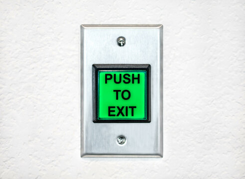 Push to exit green button mounted on white grain wall inside the apartment. Public indoor safety switch for emergency escape.