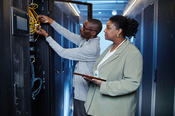 Waist up portrait of two system managers inspecting server cabinets in data center, copy space