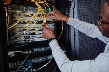 Close up of IT engineer connecting cables in server room while setting up data network, copy space