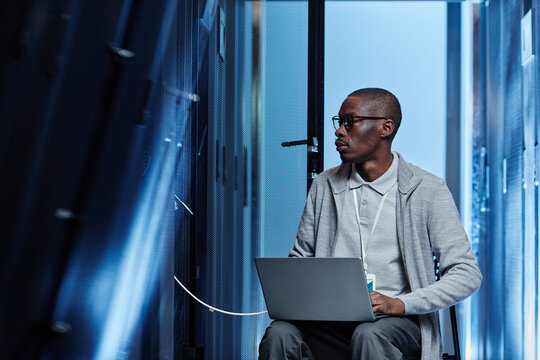 Graphic portrait of African American man working as IT engineer and setting up network in server room, copy space