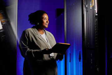 Waist up portrait of female system admin using tablet in server room lit by neon light, copy space