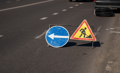 Road works sign on the road. Repair of road signs and a bypass arrow against the background of a...