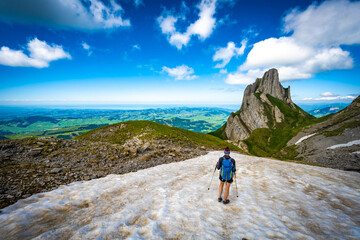 Fototapeta premium Hiker walking accross a snow field with the view on Appenzell and the lake constance