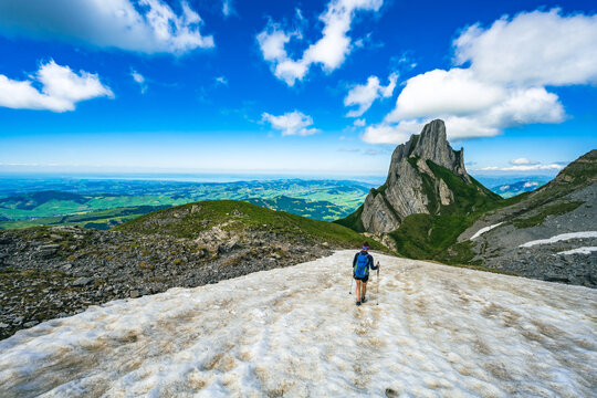 Hiker walking accross a snow field with the view on Appenzell and the lake constance
