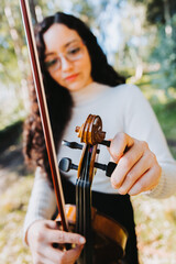 Curly brunette woman with glasses tuning her violin outside in the woods. Vertical. Selective focus.