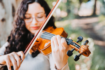 Smiling brunette woman with glasses playing violin outside in the woods. Selective focus.