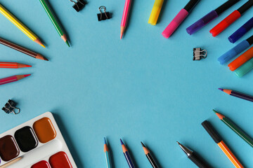 Stationary supplies on blue background framing space for text. Office accessories flat lay. The first September, back to school, education, creativity concept. Pens, pencils and paints with copyspace 