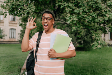 Young student mixed man hold books show okay green city park go down alley outdoors on nature. Education high school concept