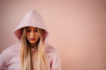 Fashion studio portrait of a happy young blonde woman in hoodie posing over pink background.