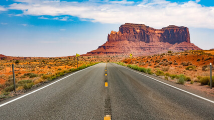 Fototapeta na wymiar A road stretches to the horizon. A mesa rises in the distance. Monument Valley, Utah.