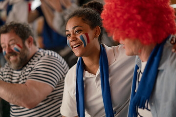 Excited football fans supproting French national team in live soccer match at stadium.