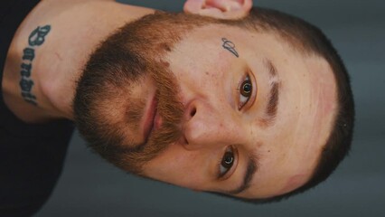 Closeup young bearded Caucasian man with tattoos on face and neck dark background . High quality 4k footage - Powered by Adobe