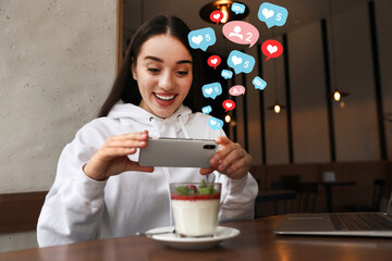 Young blogger taking picture of dessert at table in cafe