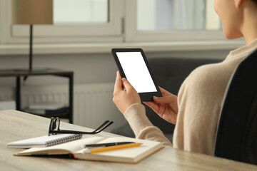 Young woman using e-book reader at wooden table indoors, closeup. Space for text © New Africa